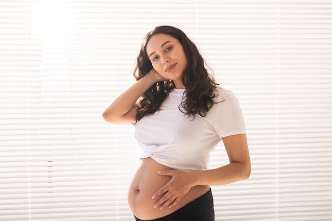 Smiling young beautiful pregnant woman touching her belly and rejoicing. Concept of positive and pleasant feelings while waiting for the baby